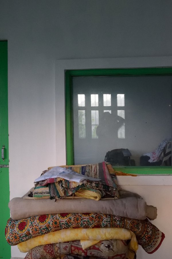 Bedding stacked outside a window, with the silhouette of the photographer reflected in the glass.